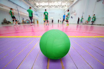 Ball is on wooden floor in gym during volleyball game, playing people out of focus