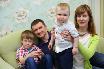 Beautiful mother, father and two little sons pose in room, focus on mom and baby