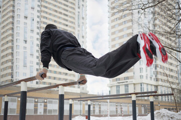 Man does exercises on parallel bars on sport playground in yard at winter, back view