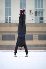Man stands on hands upside down next to building at winter day