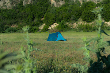 A camping tent in a green valley at the foot of mountains, creates a cozy place for relaxation.