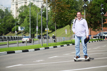 Happy man with folder rides GyroScooter on street at summer day