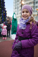 Happy little girl in purple jacket outdoor with Christmas tree