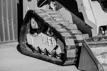 Black and white photo of compact loader track skid loader side view of the rubber tracks
