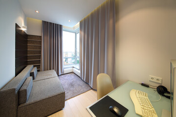 Sofa in front of a bay window with curtains and desk with a computer in the room