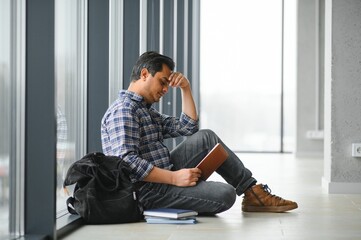 Full length of depressed boy sitting with backpack in school corridor