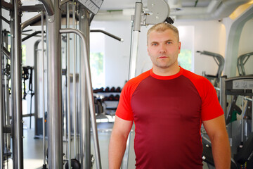Obraz premium Young strong man stands in modern gym with fitness equipment