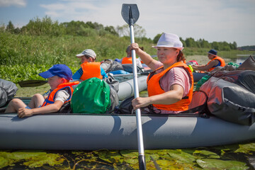 Three adults and two children in life jackets are on inflatable boats during hike at summer