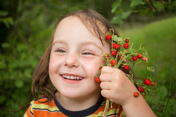 Little girl holds red wild strawberry and smiles outdoor, close up, shallow dof - Powered by Adobe