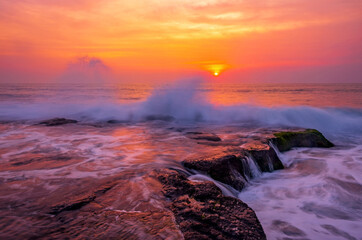 Charming atmosphere of the sea surf at sunset; waves hit the rocky shore with force, forming giant fountains of splashes
