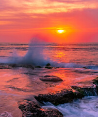 Charming atmosphere of the sea surf at sunset; waves hit the rocky shore with force, forming giant fountains of splashes