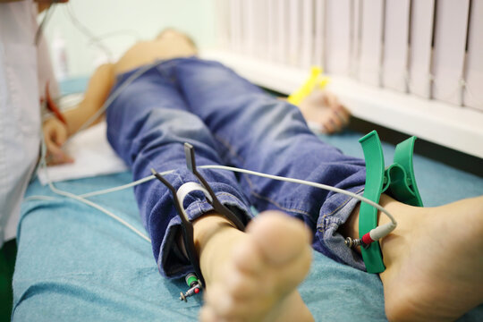 Nurse adjusts probes on young patient which lies on bed in hospital, focus on the electrodes