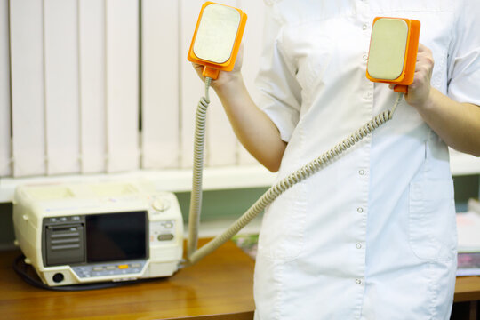 Doctor in white holds electroshock probes in hospital cabinet, noface