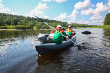 Two women and little boy sail on inflatable boats on river at sunny summer day