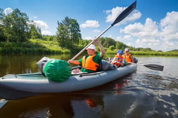 Two women with oars and little boy sail on inflatable boats on river at sunny summer day