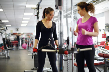 Fototapeta na wymiar Woman trainer and asian girl in sport wear trains on exerciser in modern gym