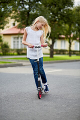 Girl with long blonde hair rides on scooter on street