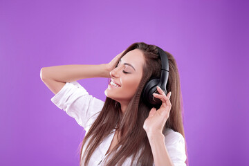 Beautiful woman listening to music using wireless headphones in studio isolated over  purple  background.Girl enjoying wireless earphones and dancing.