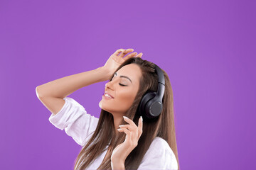 Portrait of caucasian pretty woman listening to music using wireless headphones in studio isolated over  purple  background.Girl uses wireless earphones and dancing.
