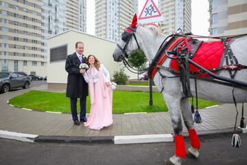Happy couple pose near coach with horse near residential buildings