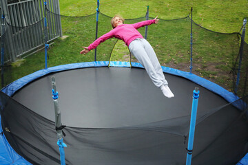 Slim smiling woman jumps on trampoline outdoor at summer day, top view