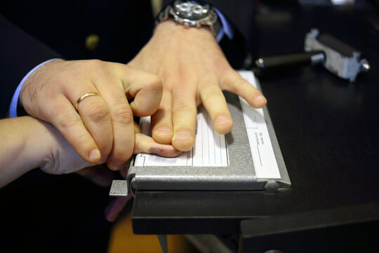 Hands of two men during fingerprinting, text translate - dactyloscopic registration, pinky