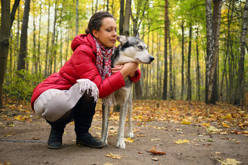 Pretty woman in red hugs husky dog in sunny autumn forest, full body