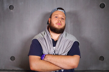 Fashionable handsome fat man with beard poses with crossed arms in studio near wall