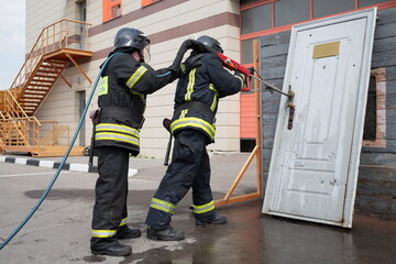 Two firefighters demonstrate lock snapping with wooden door