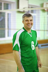 Middle age man in green sport wear stands in gym with net and smiles