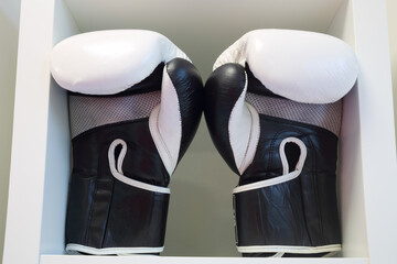 Pair of black and white leather boxing gloves on white shelf in sport center