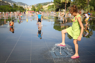 Happy pretty girl plays with dry fountain in summer town, shallow dof