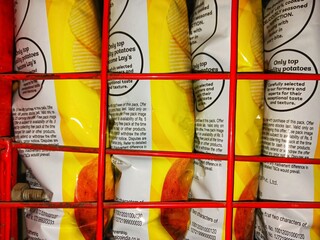 Picture of chips packets arranged tightly in a row inside a rack in a shop which can be used for illustrating super market, shop, oily foods, fast food, processed food, crowd, increasing population. 