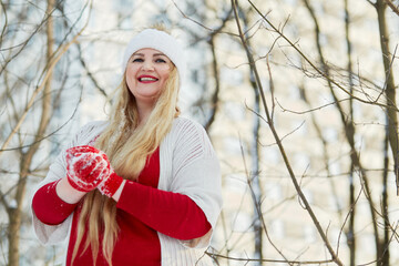 Young smiling woman stands making snowball in winter park