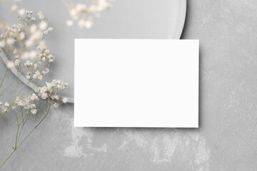 Stylish blank wedding card mockup with gypsophila flower decor and copy space on grey concrete...