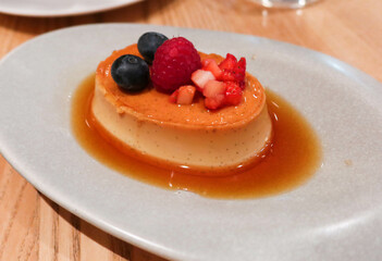 close up of milk and egg pudding with syrup. Strawberries, cranberry and blueberries as toppings on a white plate