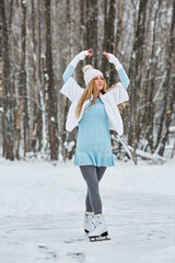 Young woman poses standing on skates at outdoor skate rink in winter park