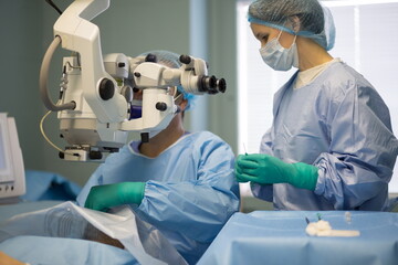  Doctor with assistent are doing eye surgery with modern microscope at the hospital