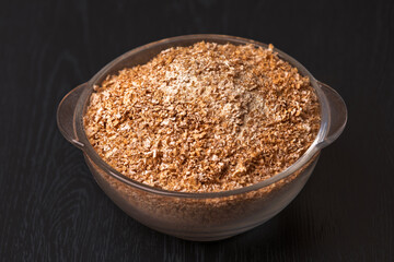 Wheat graham flour in glass bowl on black wooden background