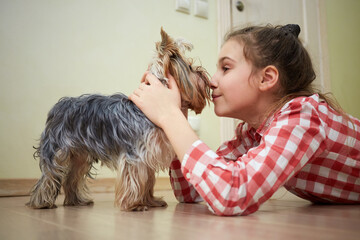 Girl rubs noses with yorkshire terrier, lying on floor in room