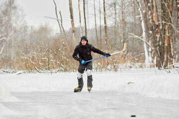 Fototapeta na wymiar Young man plays hockey at outdoor skating rink in park