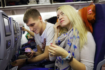 Man with smartphone and woman with headphones sit in airplane before flight