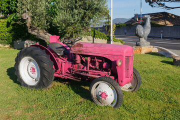  Retro pink tractor and stone sculpture of rooster on lawn next to carriageway - obrazy, fototapety, plakaty