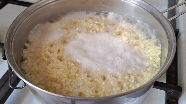 Millet porridge boiling in a steel pan closeup, steaming hot water. Cooked on a gas stove