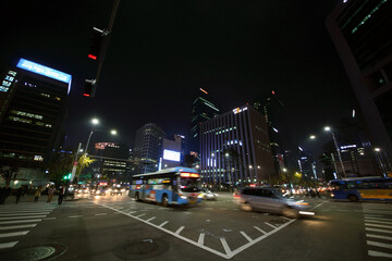 Fototapeta na wymiar People crossing road on crosswalk and cars move at night. Pedestrians in Seoul can now more safely get to streets of central areas
