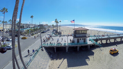  People walk by Manhattan Beach Pier along sandy beach at sunny day. Aerial view. Pier was built in 1920.