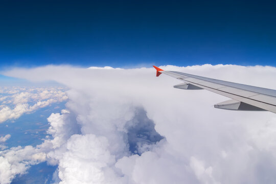 Wing of flying airplane at clouds in blue sky, view from window