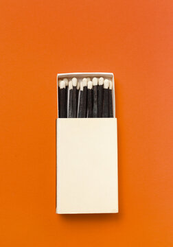 Black matches in a box on a orange background.