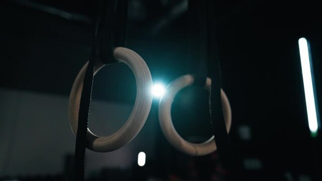 Close up shot - Gymnastic rings gently swinging in the gym on a dark background with mood lightening