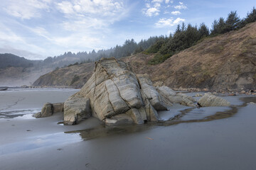 A large rock sits on a beach, surrounded by water and trees